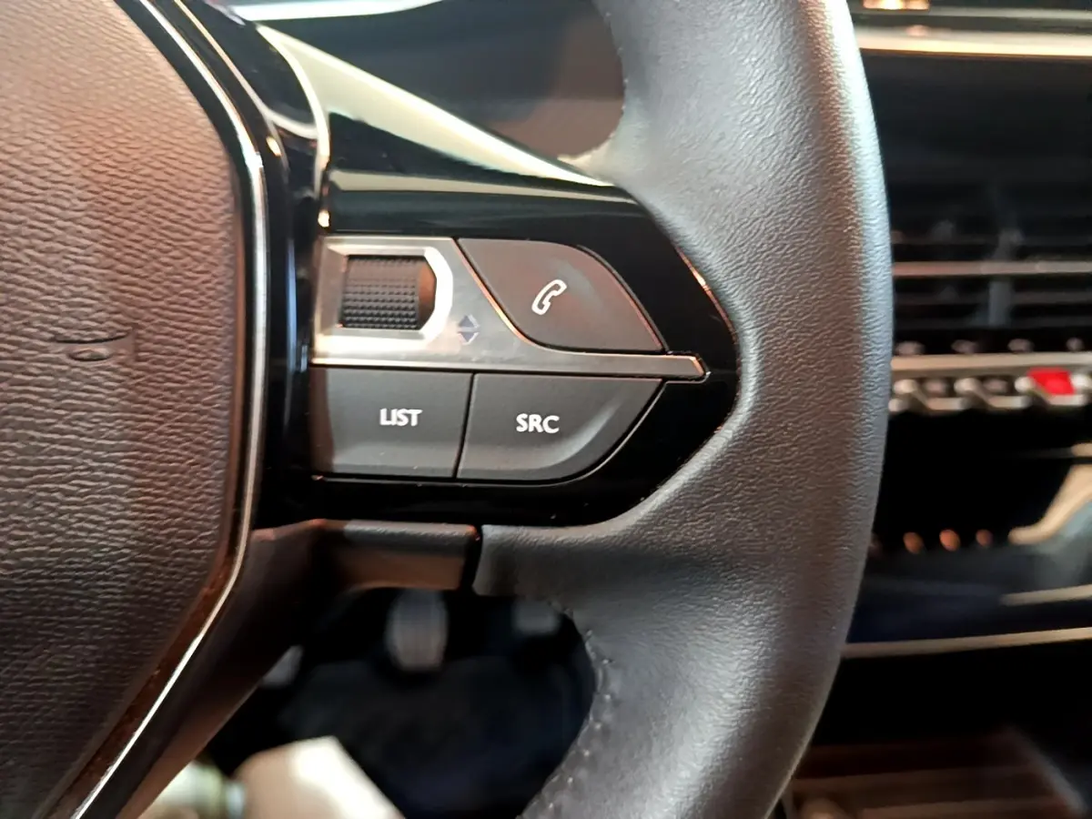 Gros plan sur le volant cuir multifonctions de la Peugeot 208 jaune, avec commandes audio et téléphone intégrées.