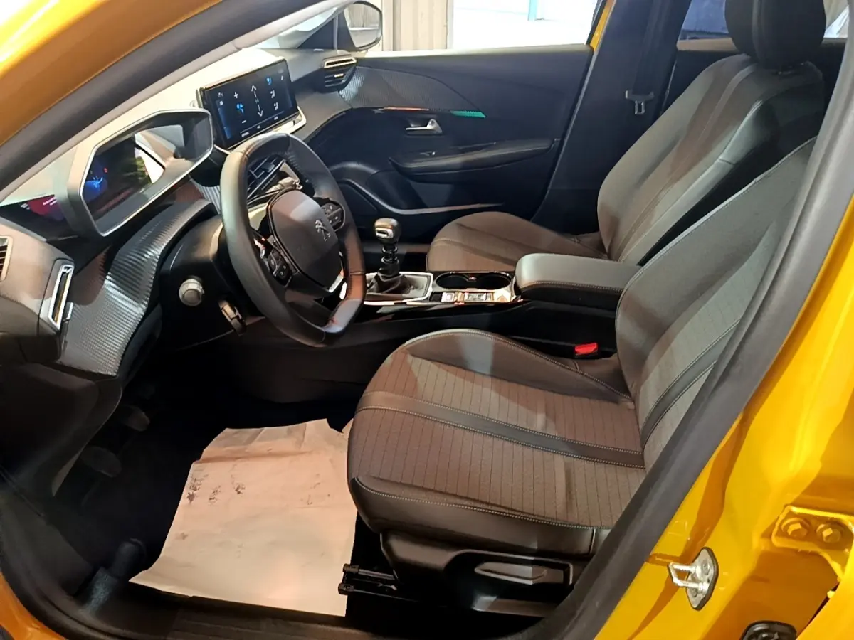 Intérieur avant droit d’une Peugeot 208 jaune 2023, volant cuir multifonctions et tableau de bord digital.