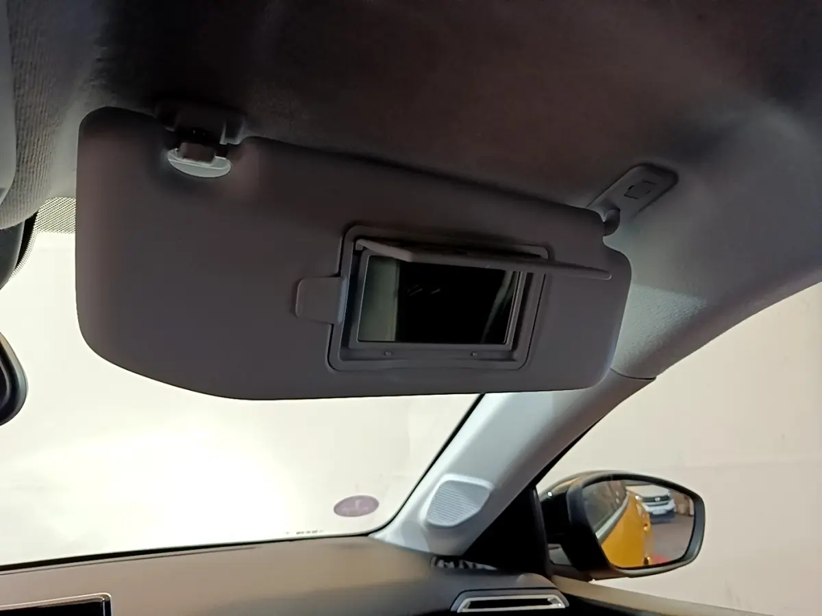 Vue intérieure côté conducteur du pare-soleil avec miroir ouvert, reflet du Peugeot 208 jaune dans le rétroviseur extérieur.