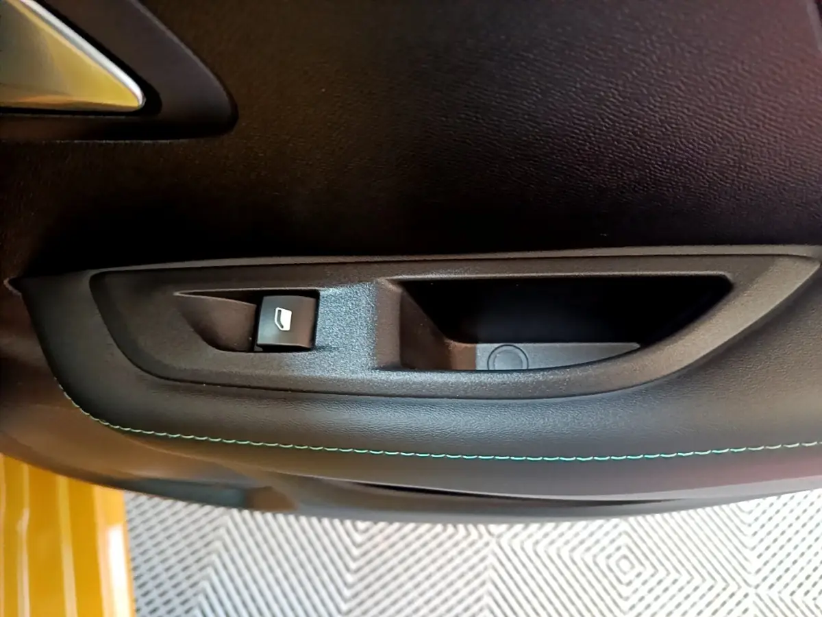 Gros plan sur la commande de lève-vitre côté conducteur avec surpiqûre bleue sur la porte noire d’une Peugeot 208 jaune.