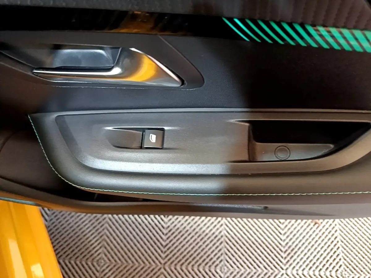 Gros plan sur la poignée intérieure côté gauche de la porte noire avec surpiqûres vertes d’une Peugeot 208 jaune.
