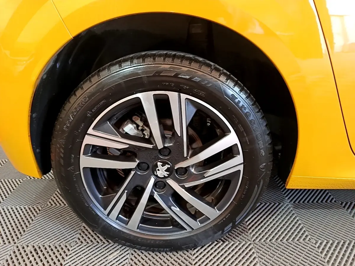 Gros plan sur la roue avant droite de la Peugeot 208 jaune, avec jante alliage noire et argentée au design moderne.