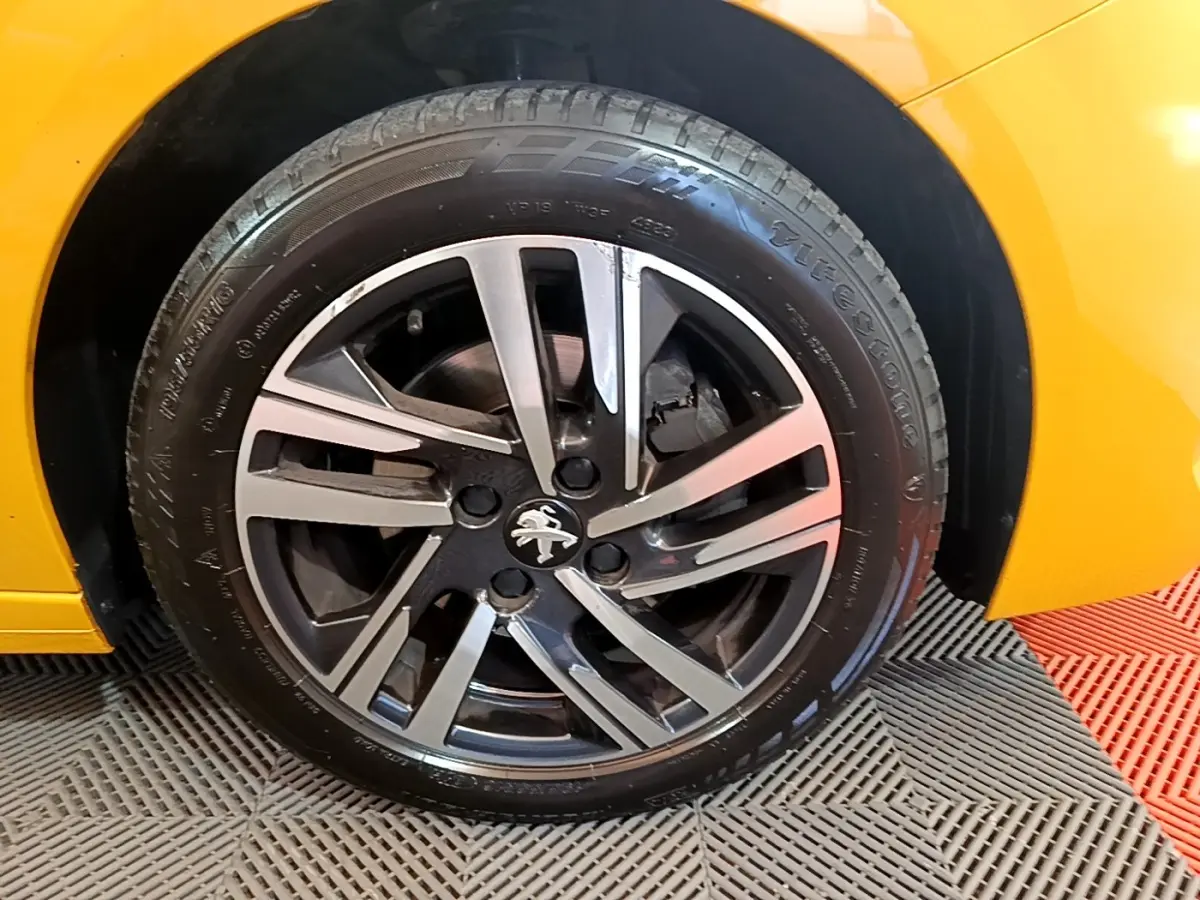 Gros plan sur la roue avant droite d'une Peugeot 208 jaune 2023 avec jante alliage bicolore et logo lion.