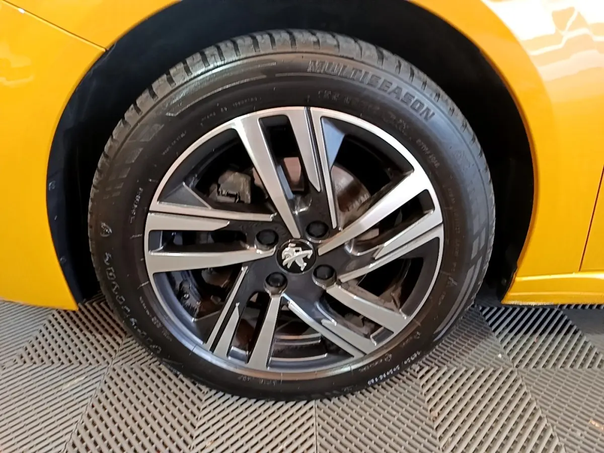 Gros plan sur la roue avant droite de la Peugeot 208 jaune avec jante alliage bicolore et logo lion central.