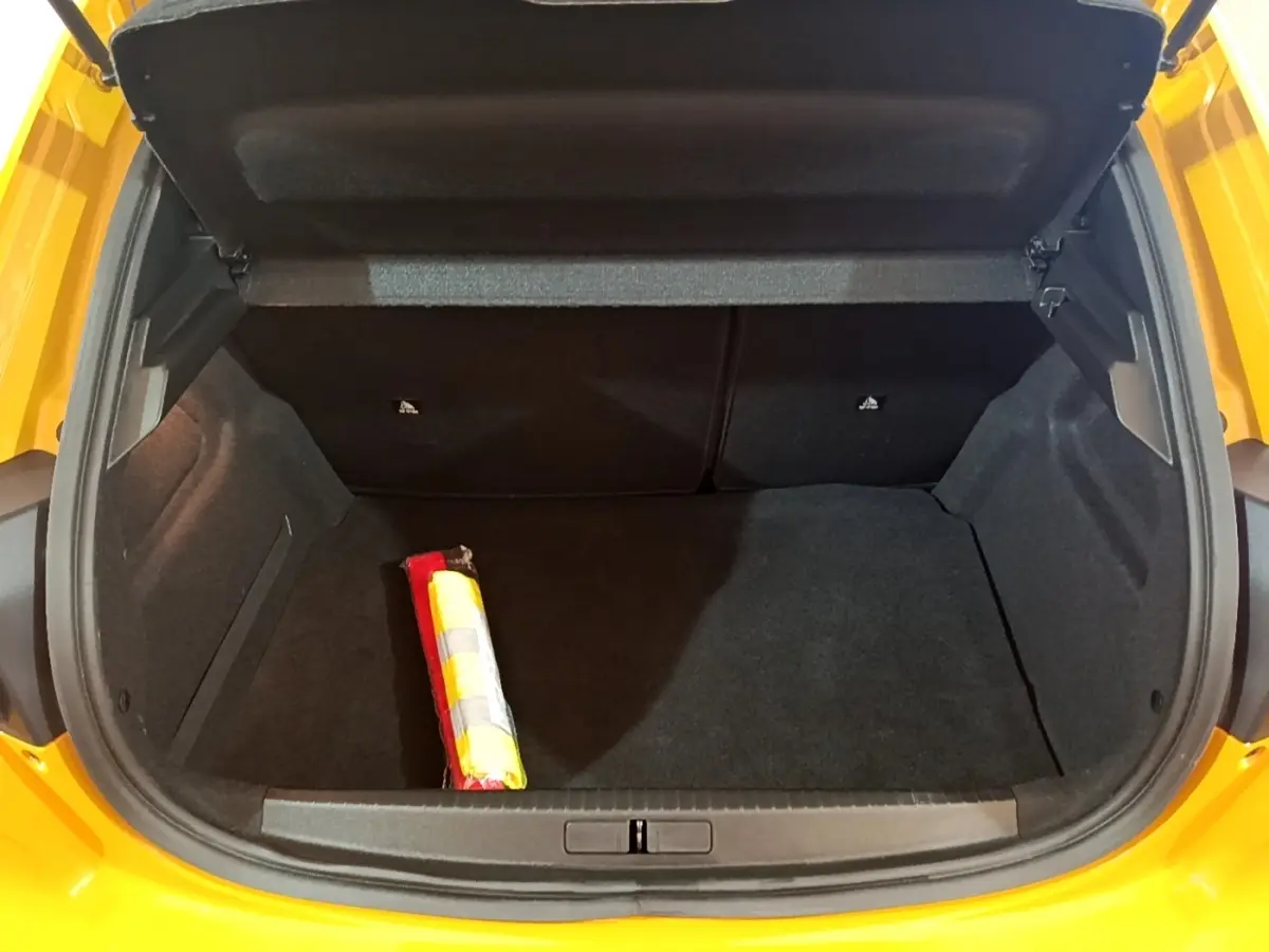 Coffre ouvert vu de l'arrière d'une Peugeot 208 jaune 2023, avec un triangle de signalisation visible à l'intérieur.