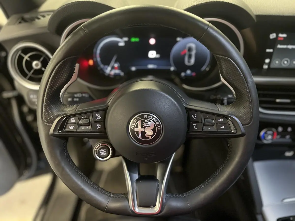 Vue rapprochée du volant sport en cuir noir de l'Alfa Romeo Stelvio 2024 avec commandes intégrées et tableau de bord digital.