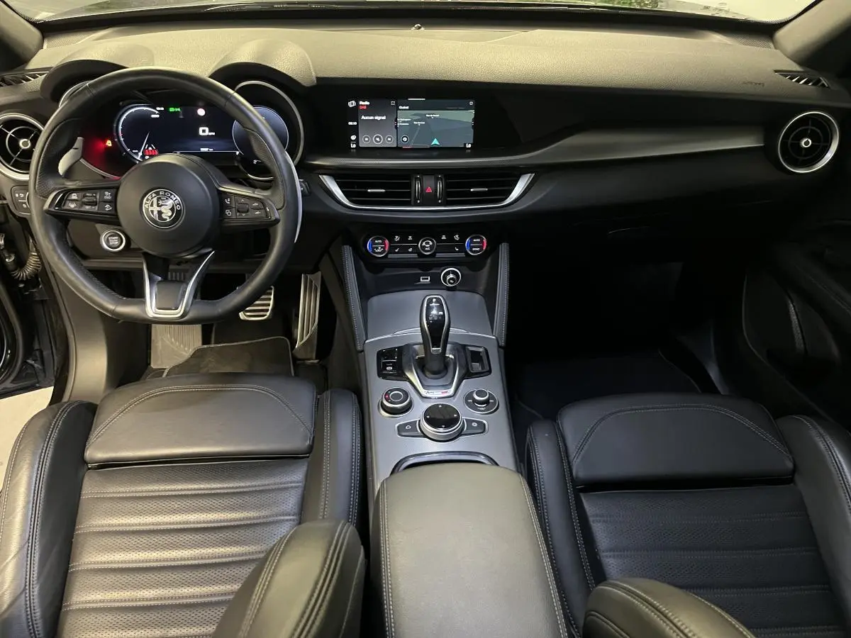 Vue intérieure frontale de l'Alfa Romeo Stelvio Veloce 2024, avec sièges sport cuir noir et console centrale moderne.
