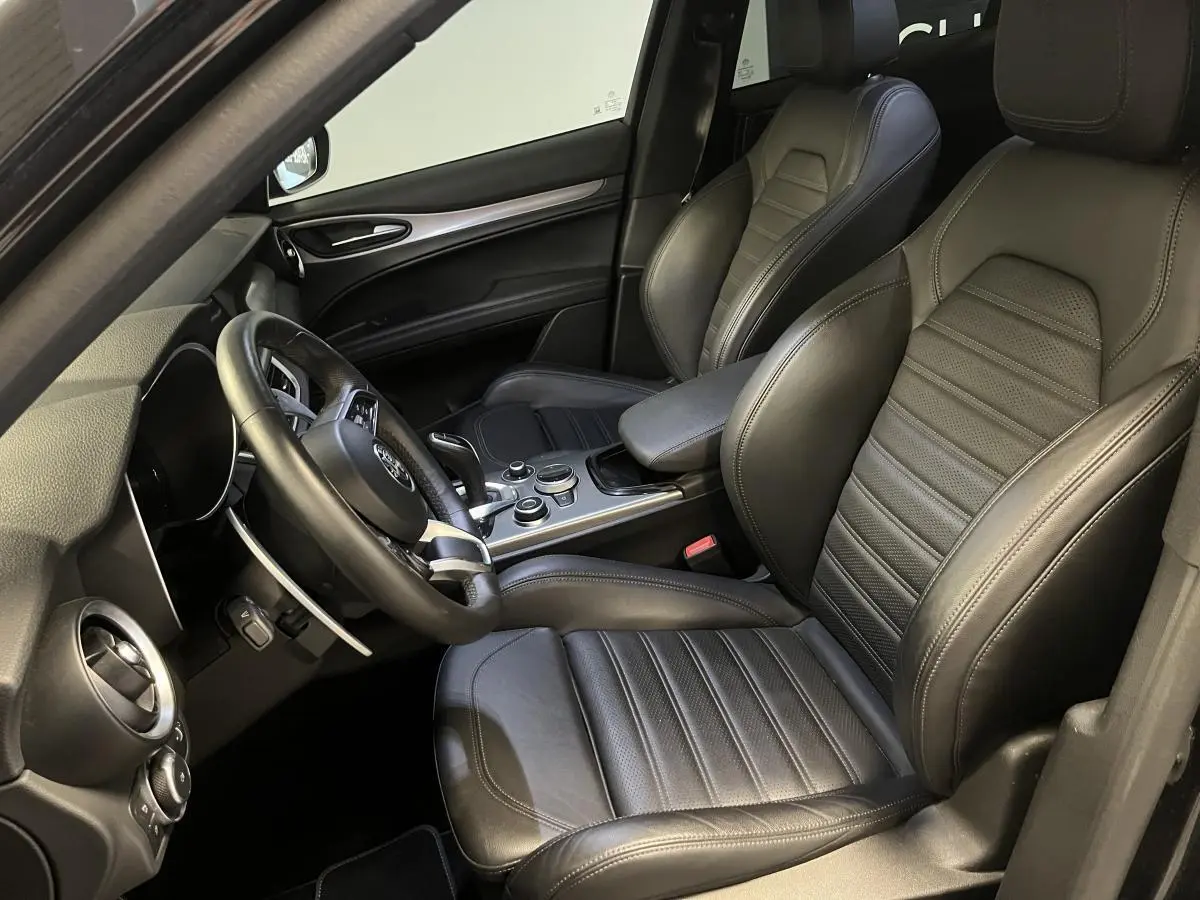 Vue intérieure côté conducteur de l'Alfa Romeo Stelvio Veloce 2024 avec sièges sport cuir noir et volant sport.