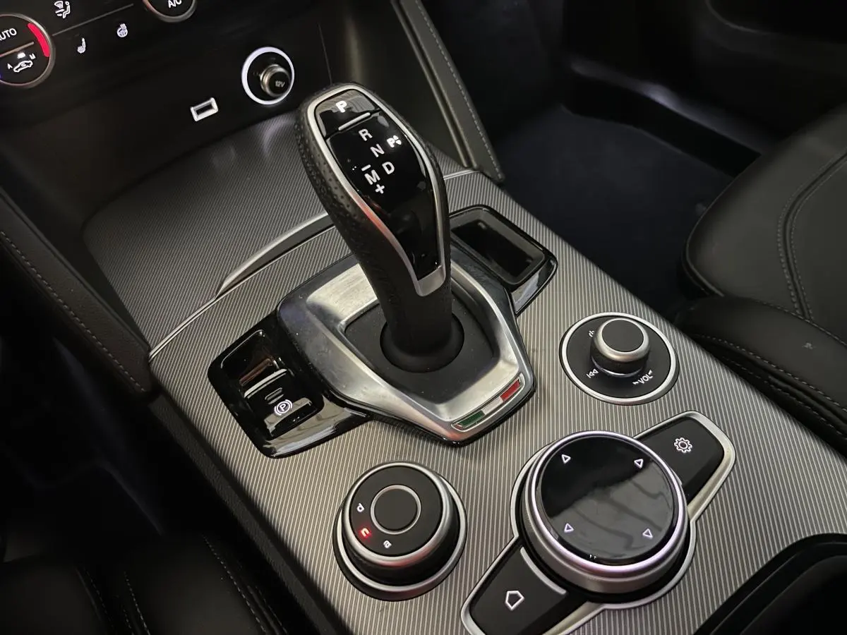 Gros plan sur la console centrale de l'Alfa Romeo Stelvio 2024, avec levier de vitesses automatique et commandes circulaires.