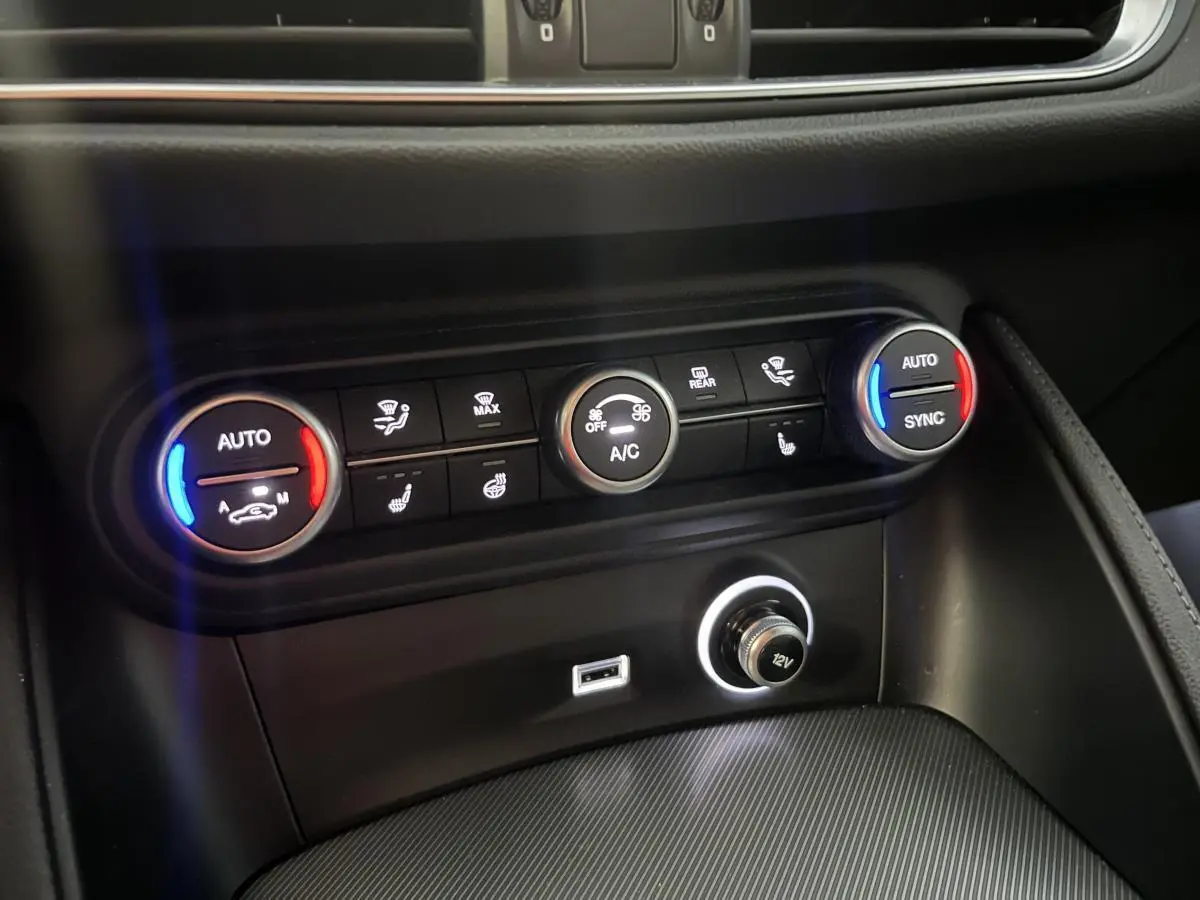 Gros plan sur la console centrale de l'Alfa Romeo Stelvio 2024, boutons de climatisation avec éclairage bleu et rouge.