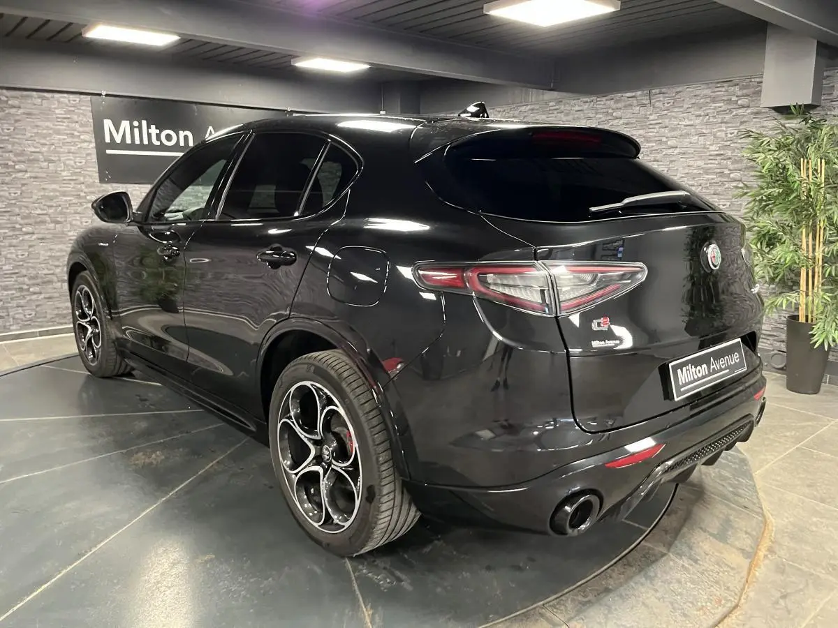 Vue 3/4 arrière droite d'un Alfa Romeo Stelvio Veloce noir Vulcano avec jantes 20 pouces et double sortie d'échappement noire.