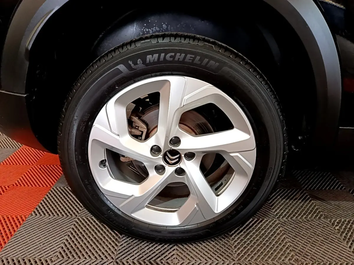 Gros plan sur la roue arrière droite noire d’un Citroën C5 Aircross hybride rechargeable 2022 sur sol carrelé rouge et gris.