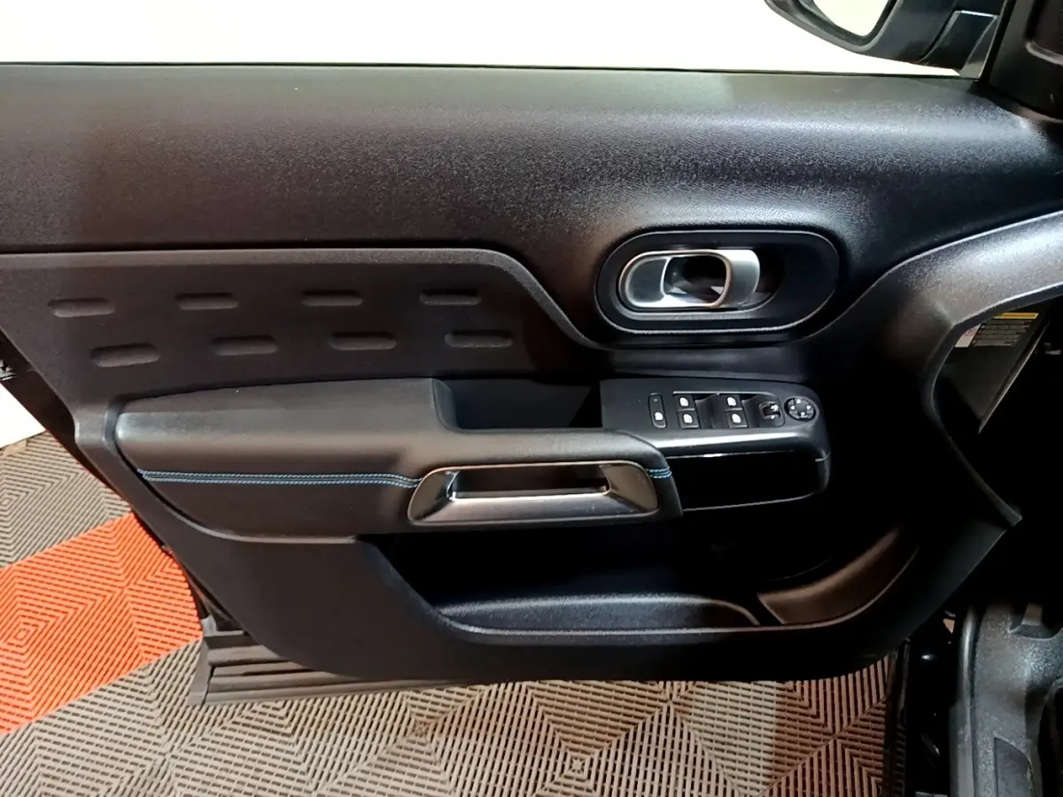 Vue intérieure côté gauche de la porte noire du Citroën C5 Aircross hybride avec commandes électriques et poignée chromée.