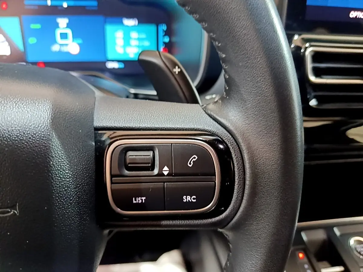 Gros plan sur les commandes gauche du volant cuir noir du Citroën C5 Aircross hybride rechargeable 2022, avec écran tactile en arrière-plan.