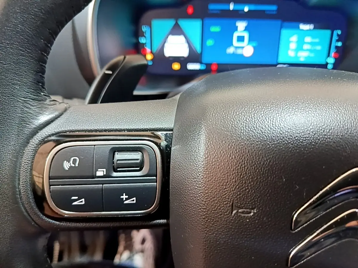 Gros plan sur le volant noir de la Citroën C5 Aircross hybride avec commandes intégrées et tableau de bord numérique en arrière-plan.