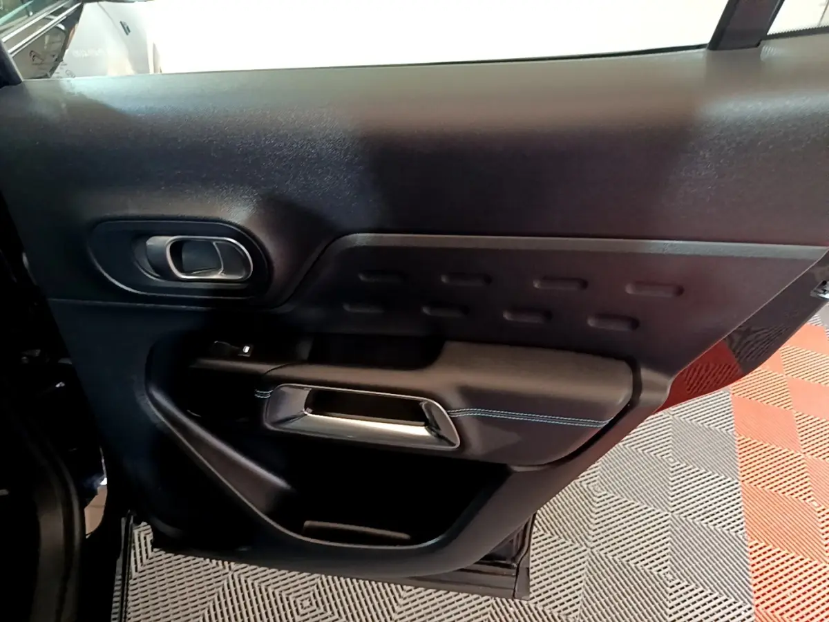 Vue intérieure de la porte arrière gauche noire du Citroën C5 Aircross hybride rechargeable avec poignée argentée et surpiqûres bleues.