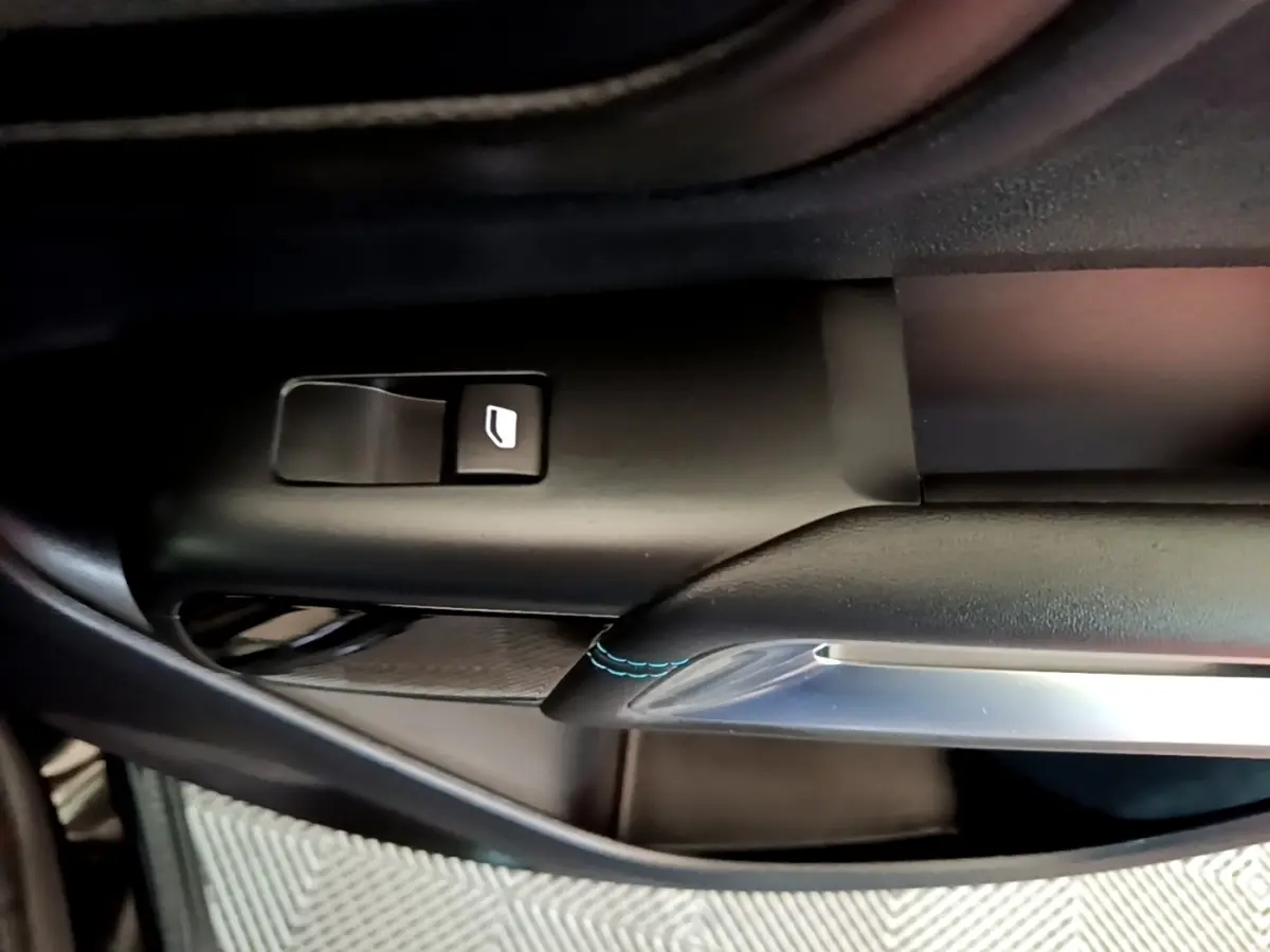 Détail de la commande de lève-vitre côté conducteur avec surpiqûres bleues sur garniture noire du Citroën C5 Aircross hybride.