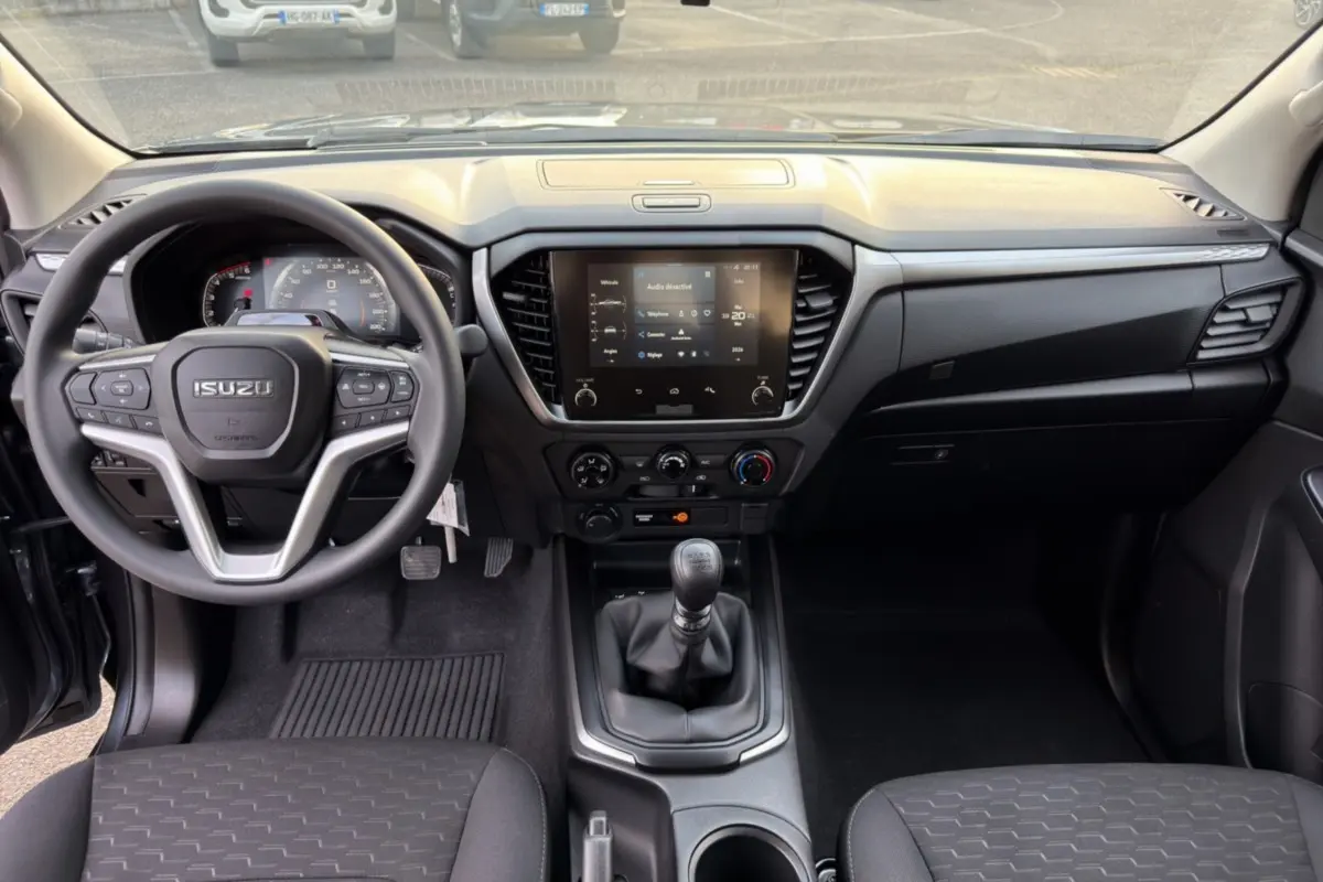 Vue intérieure avant de l'Isuzu D-MAX 2026 avec tableau de bord noir et écran tactile central.