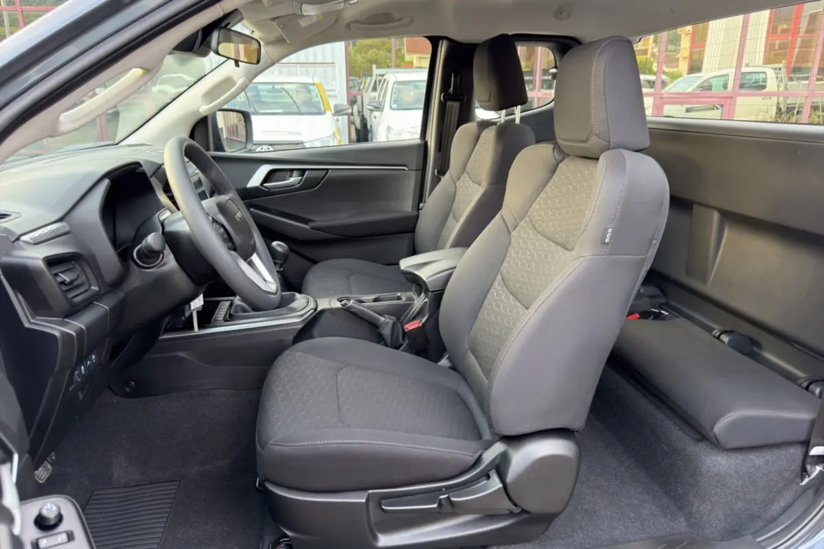 Vue intérieure côté conducteur du pick-up Isuzu D-MAX 2.2 TD 164 Space Evolution, sièges tissu gris et accoudoir central.