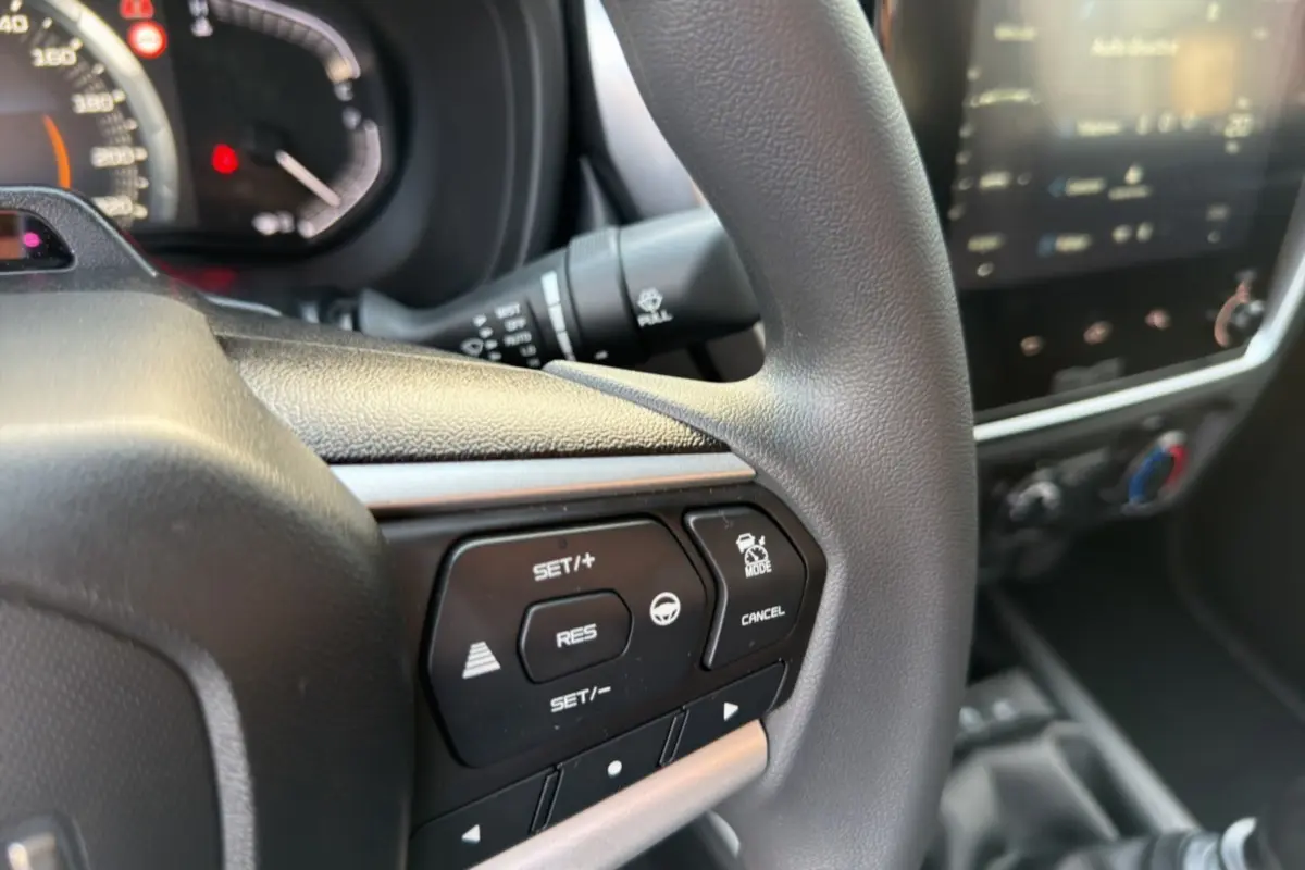 Gros plan sur le volant multifonctions noir de l'Isuzu D-MAX 2026 avec commandes de régulateur et écran tactile flou en arrière-plan.