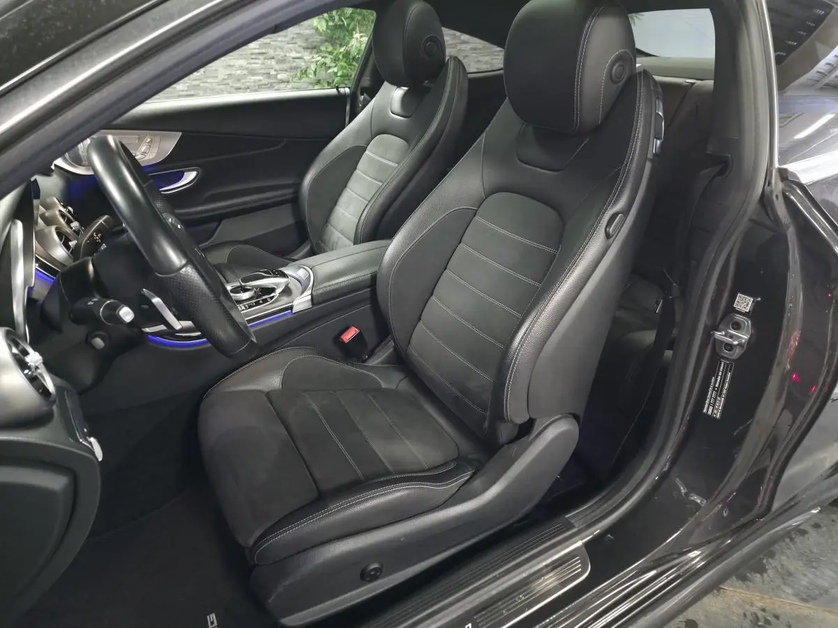 Vue intérieure côté conducteur de la Mercedes Classe C Coupé gris, sièges sport noirs avec surpiqûres blanches et éclairage d'ambiance bleu.