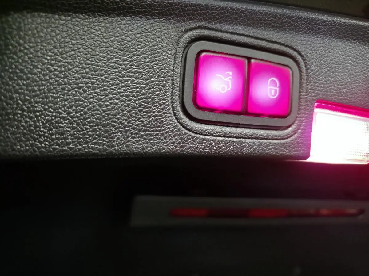 Gros plan sur les boutons lumineux de déverrouillage du coffre et de verrouillage central dans le coffre d'une Mercedes Classe C Coupé gris.