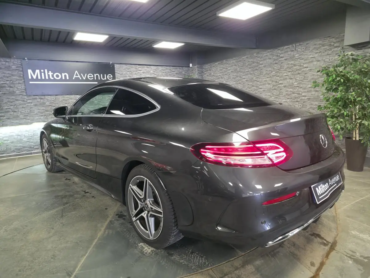 Vue 3/4 arrière droite d'une Mercedes Classe C Coupé gris métallisé avec jantes AMG 18 pouces et feux LED allumés.