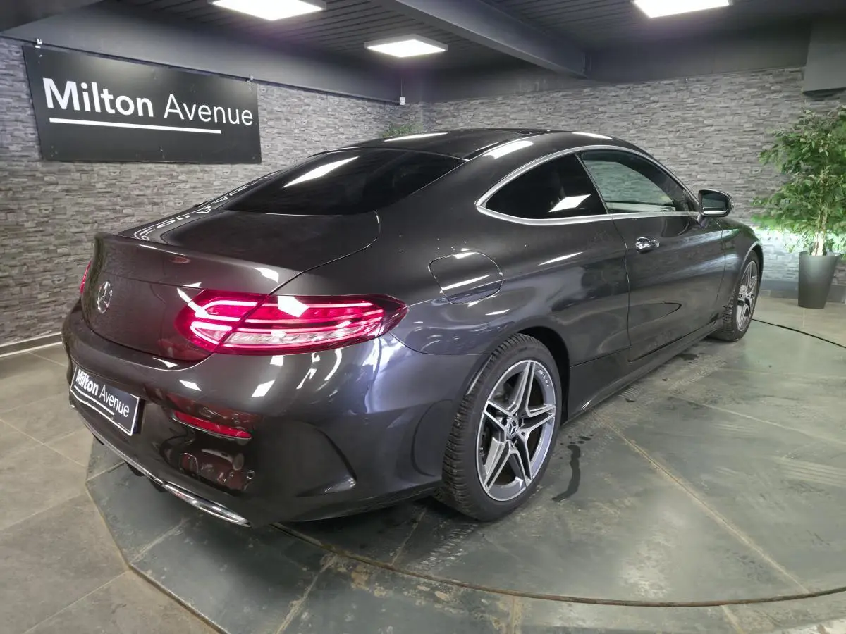 Vue 3/4 arrière droit d'une Mercedes Classe C Coupé gris métallisé avec jantes AMG 18 pouces et feux arrière LED allumés.