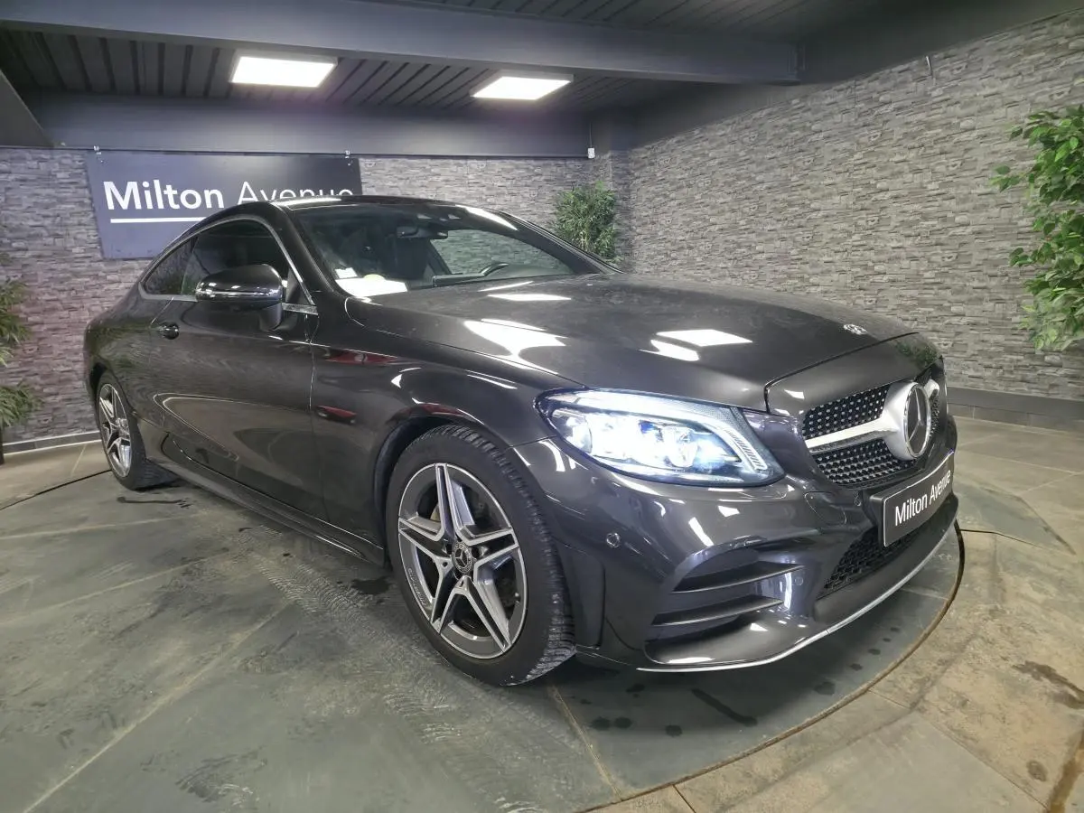 Mercedes Classe C Coupé gris métallisé en 3/4 avant droit avec jantes AMG 18 pouces et projecteurs LED allumés.