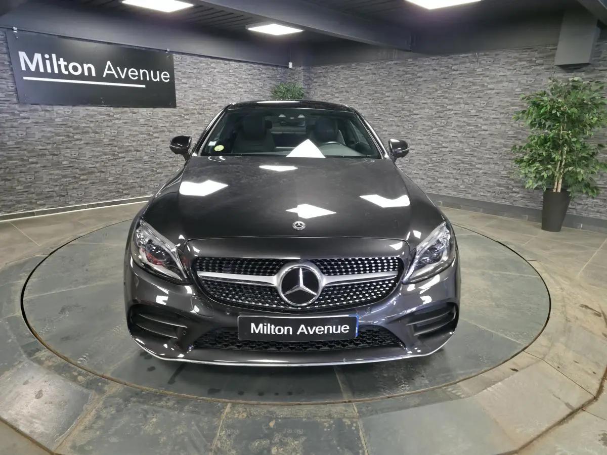 Mercedes Classe C Coupé gris métallisé vu de face dans un showroom avec calandre AMG et logo étoile bien visibles.