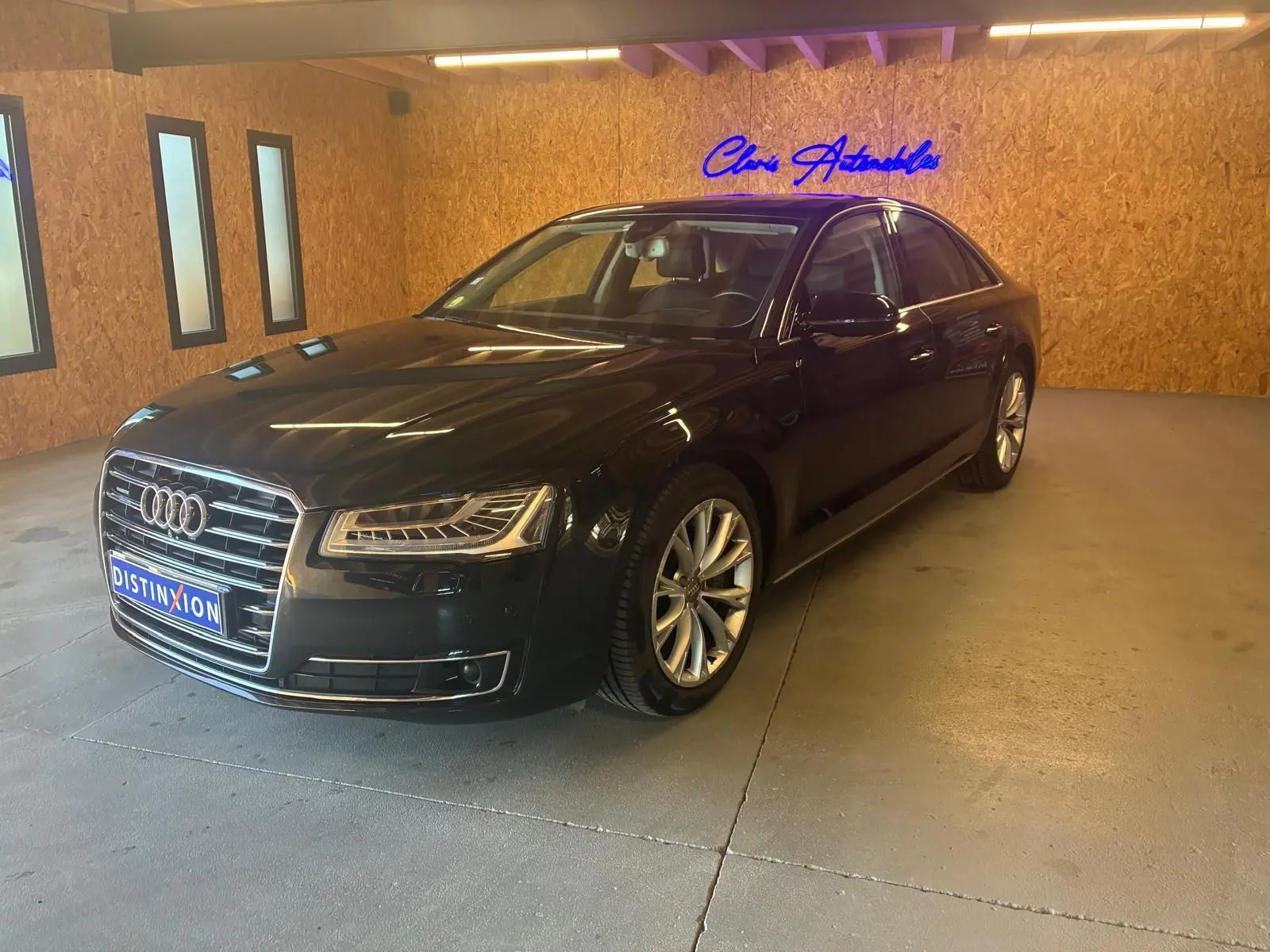 Audi A8 3.0 TDI noire vue en 3/4 avant droit dans un showroom avec éclairage chaud et murs en bois.