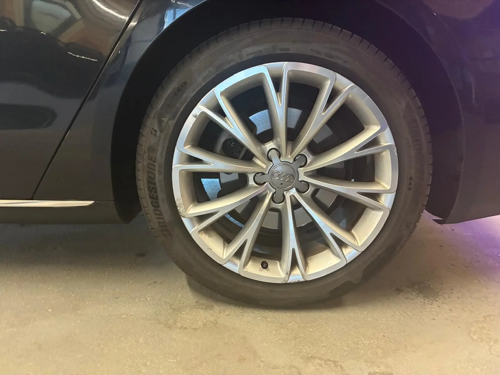 Gros plan sur la roue avant droite d'une Audi A8 noire 2016, jante alliage à design multiple branches.