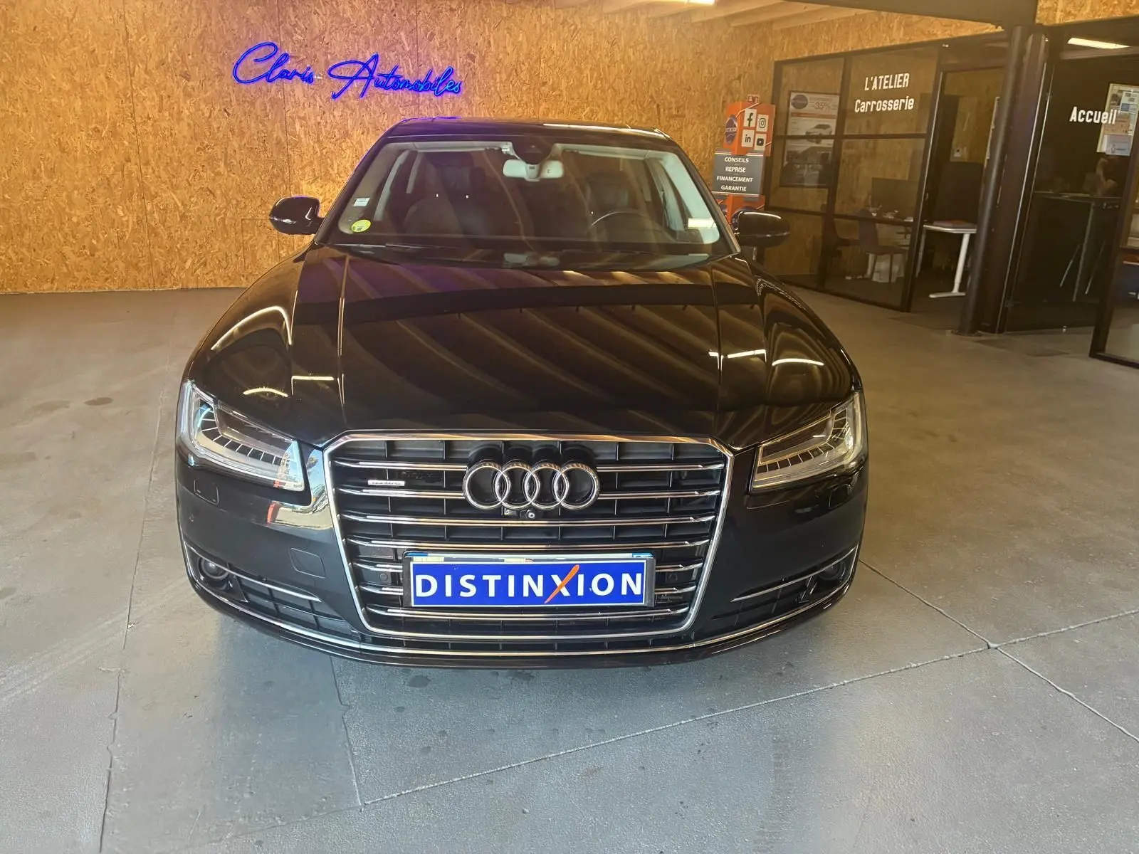 Vue avant d'une Audi A8 noire 2016 avec calandre chromée et plaques Distinxion dans un showroom.