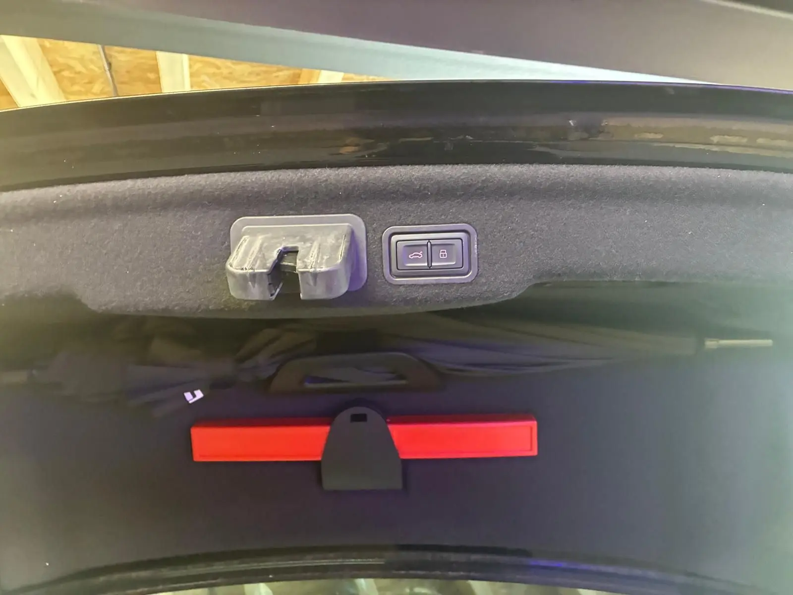 Détail intérieur du coffre de l'Audi A8 2016 noir, montrant les boutons d'ouverture et verrouillage du hayon.