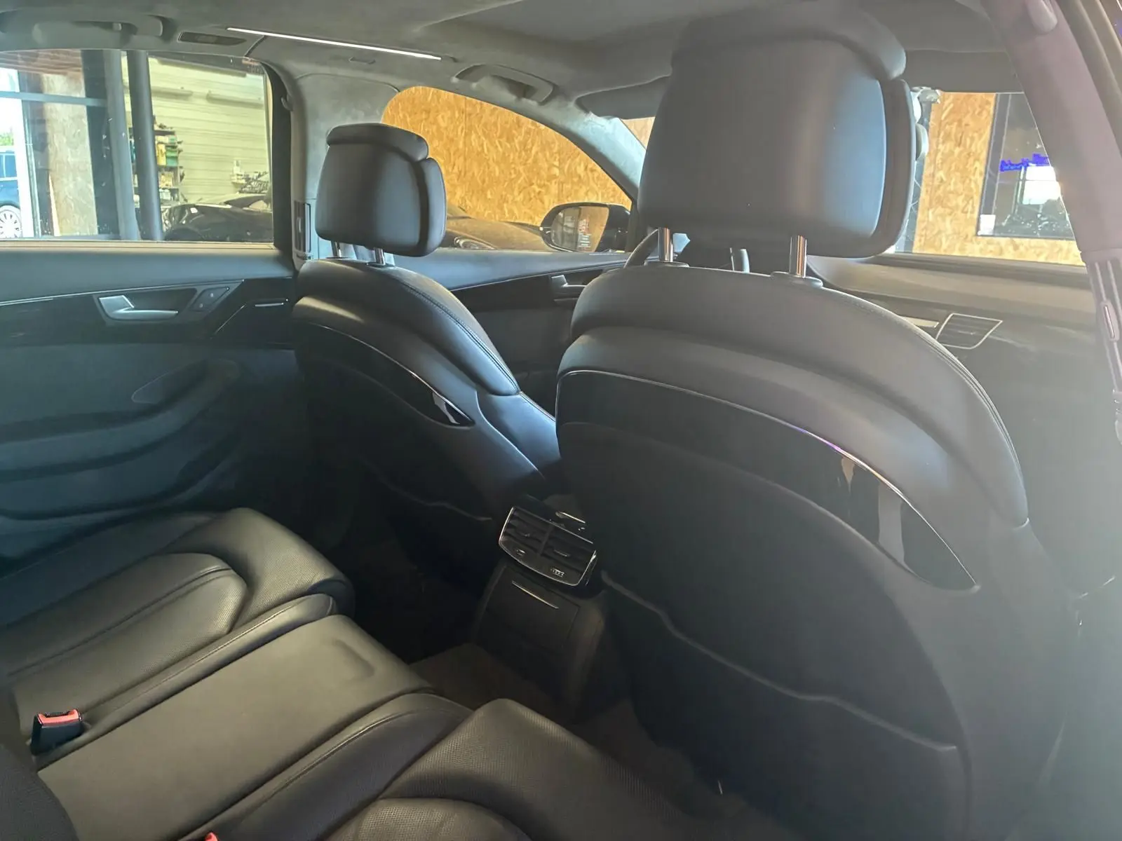 Vue intérieure arrière de l'Audi A8 2016 noire, montrant les sièges en cuir et la console centrale avec aérateurs.
