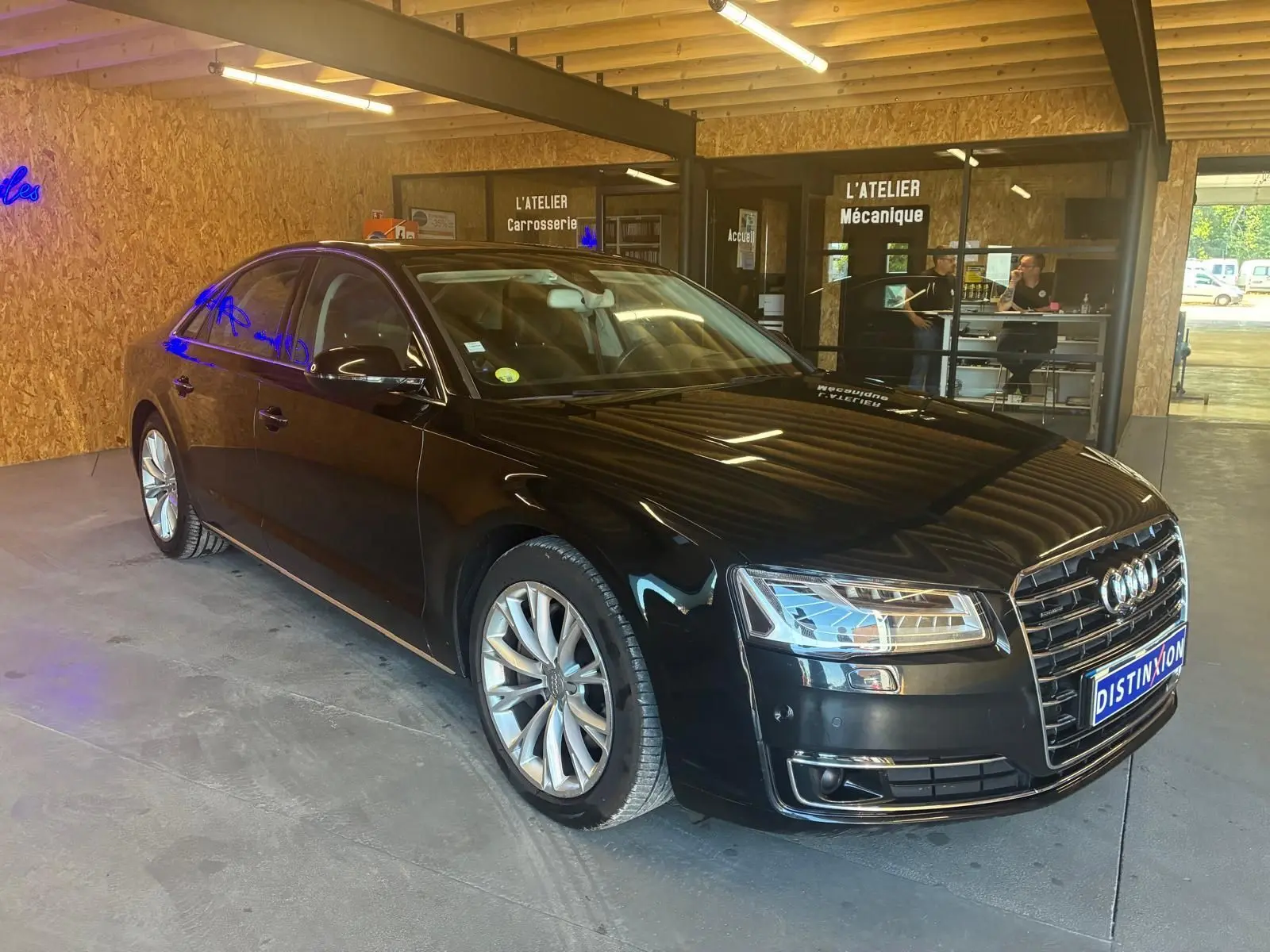 Audi A8 3.0 TDI noire vue en 3/4 avant droit dans un atelier avec reflets lumineux sur la carrosserie.