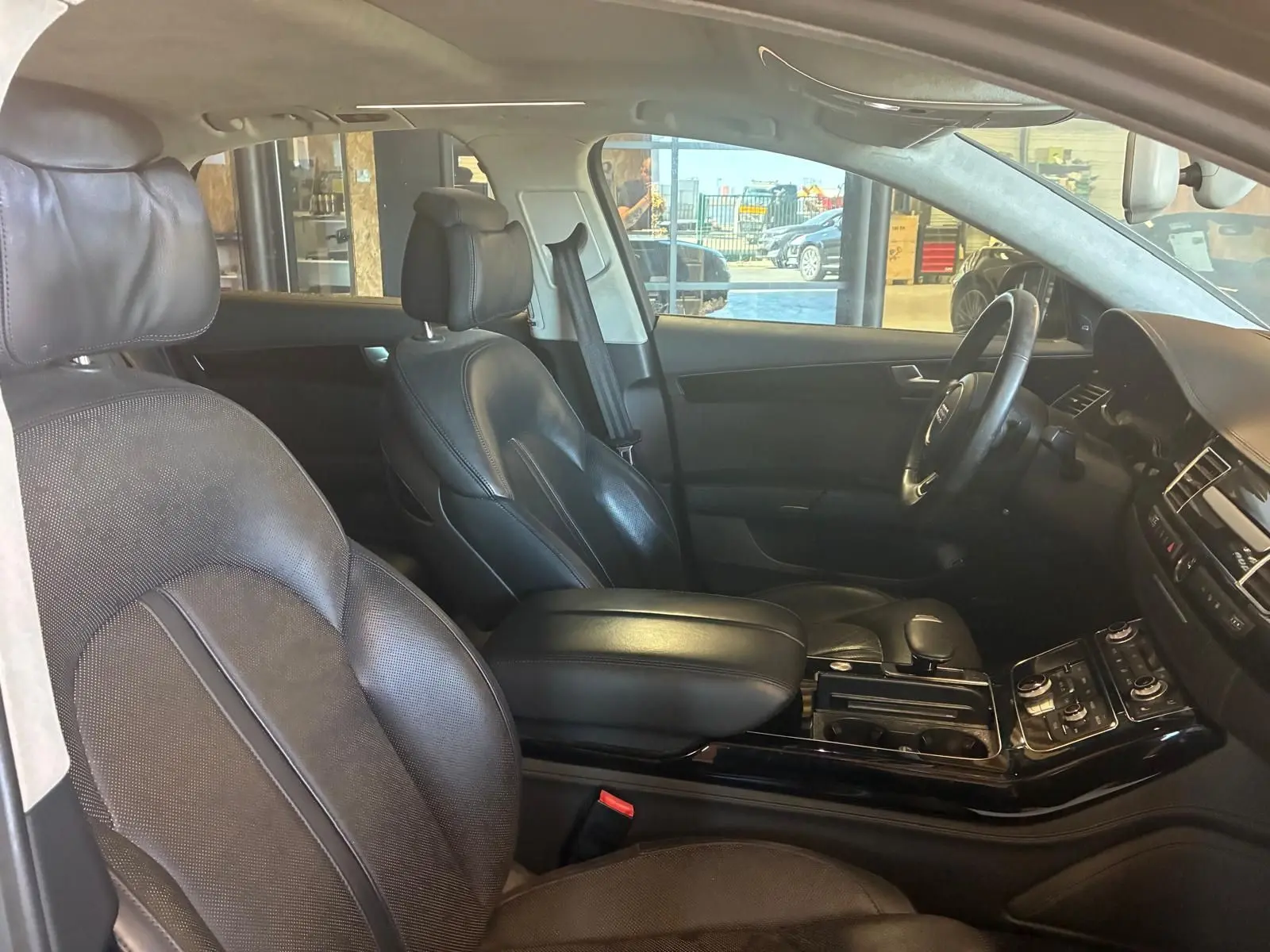 Vue intérieure côté conducteur de l'Audi A8 2016, sièges cuir noirs et console centrale avec commandes intégrées.