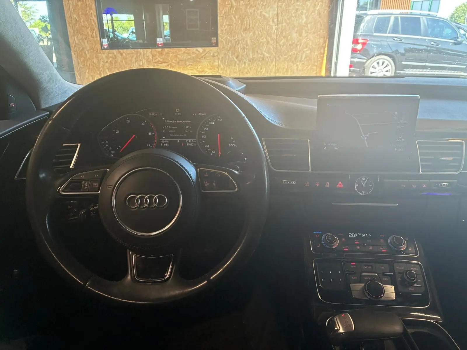 Vue intérieure centrée sur le volant et le tableau de bord d'une Audi A8 noire, avec écran de navigation et commandes visibles.