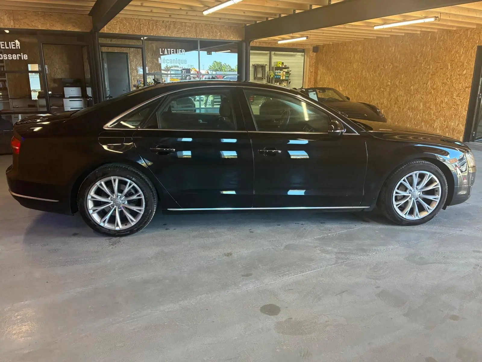 Audi A8 3.0 TDI 2016 noir vue de profil côté gauche, avec jantes alliage et intérieur visible en atelier.