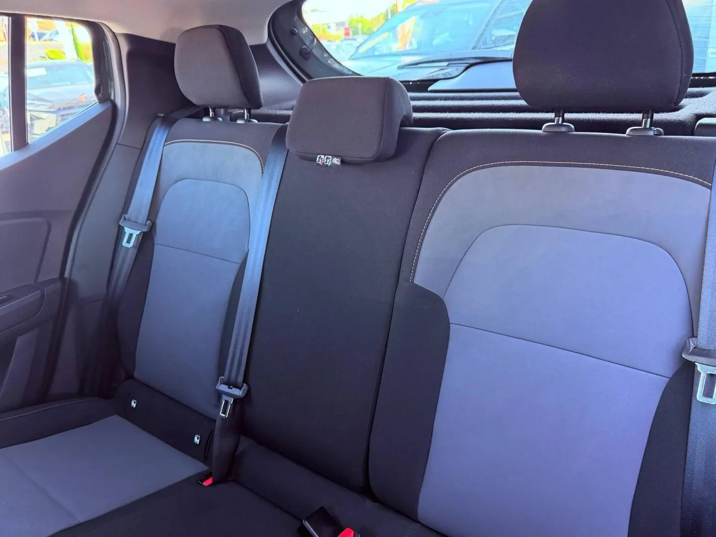 Vue intérieure sur la banquette arrière en tissu brun cuivré de la Dacia Sandero 2025, avec appuie-têtes et ceintures visibles.