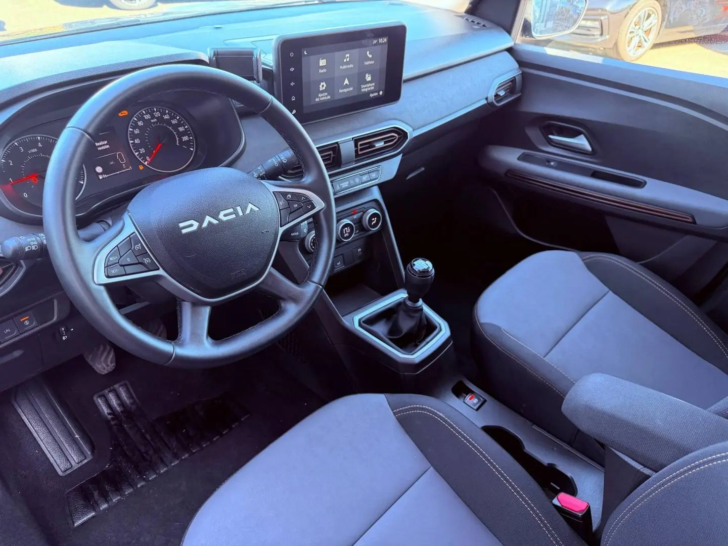 Intérieur de la Dacia Sandero 2025 vu côté conducteur, volant multifonction, écran tactile et sièges tissu brun cuivré.