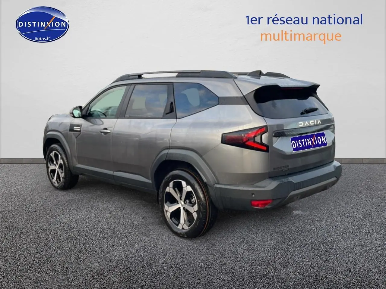 Vue 3/4 arrière droite du Dacia Bigster gris schiste avec jantes diamantées et barres de toit noires visibles.