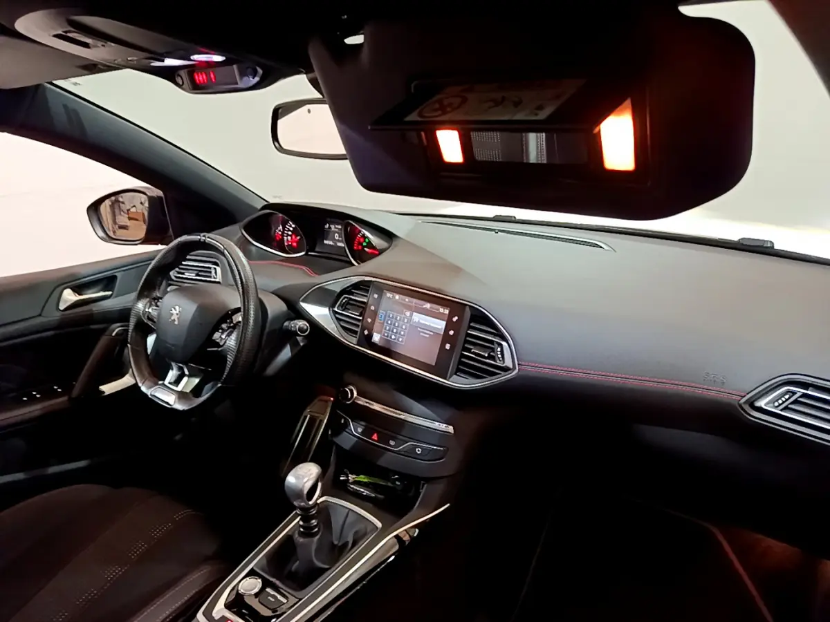 Vue intérieure côté conducteur de la Peugeot 308 gris foncé, mettant en valeur le tableau de bord et la console centrale avec écran tactile.
