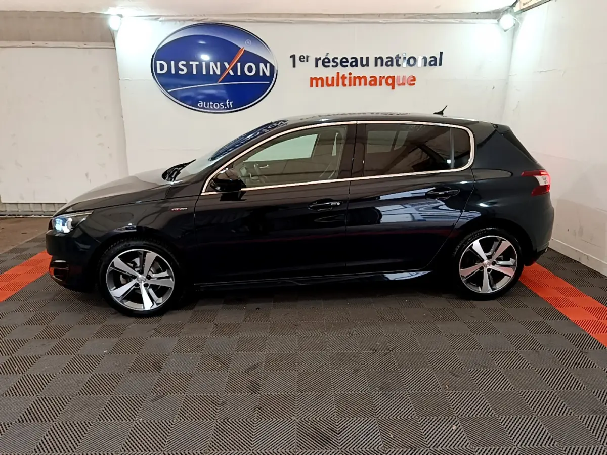 Peugeot 308 gris foncé vue de profil côté gauche, avec jantes alliage et feux avant allumés.