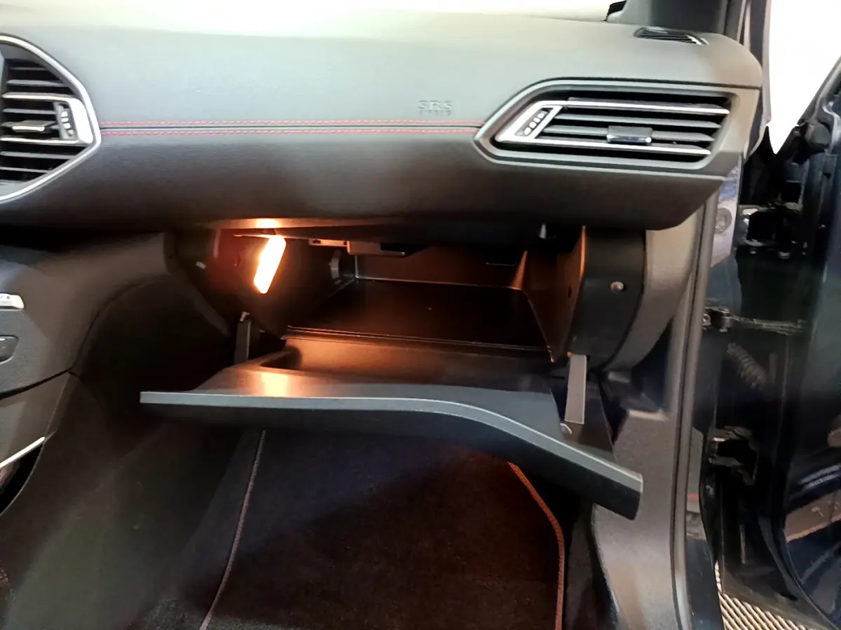 Gros plan sur la boîte à gants ouverte côté passager d’une Peugeot 308 gris foncé avec éclairage intérieur.