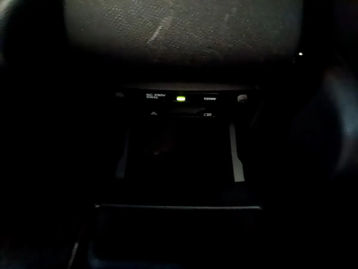 Détail de la prise 12V et prise secteur 230V 120W dans l'habitacle sombre d'une Peugeot 308 gris foncé.