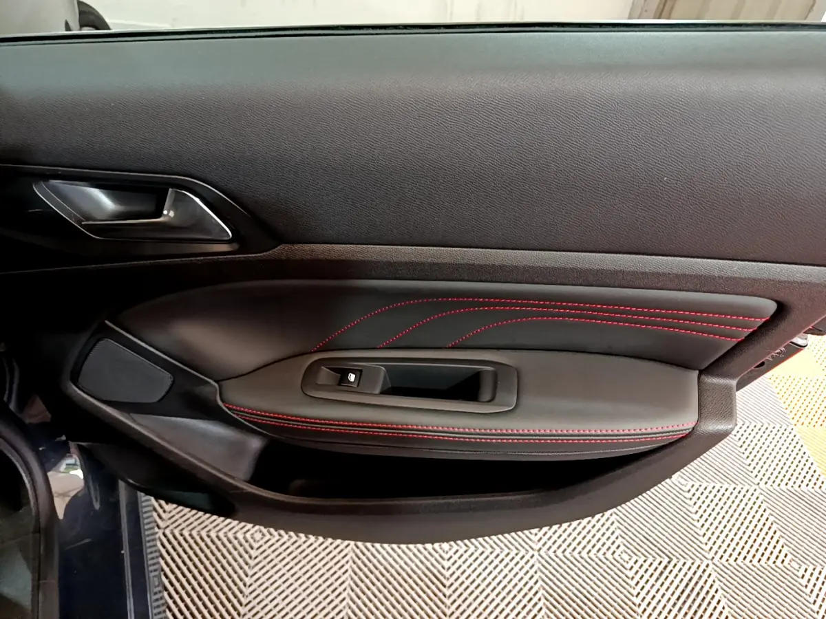 Vue intérieure du panneau de porte côté gauche de la Peugeot 308 gris foncé avec surpiqûres rouges et commande de lève-vitre.