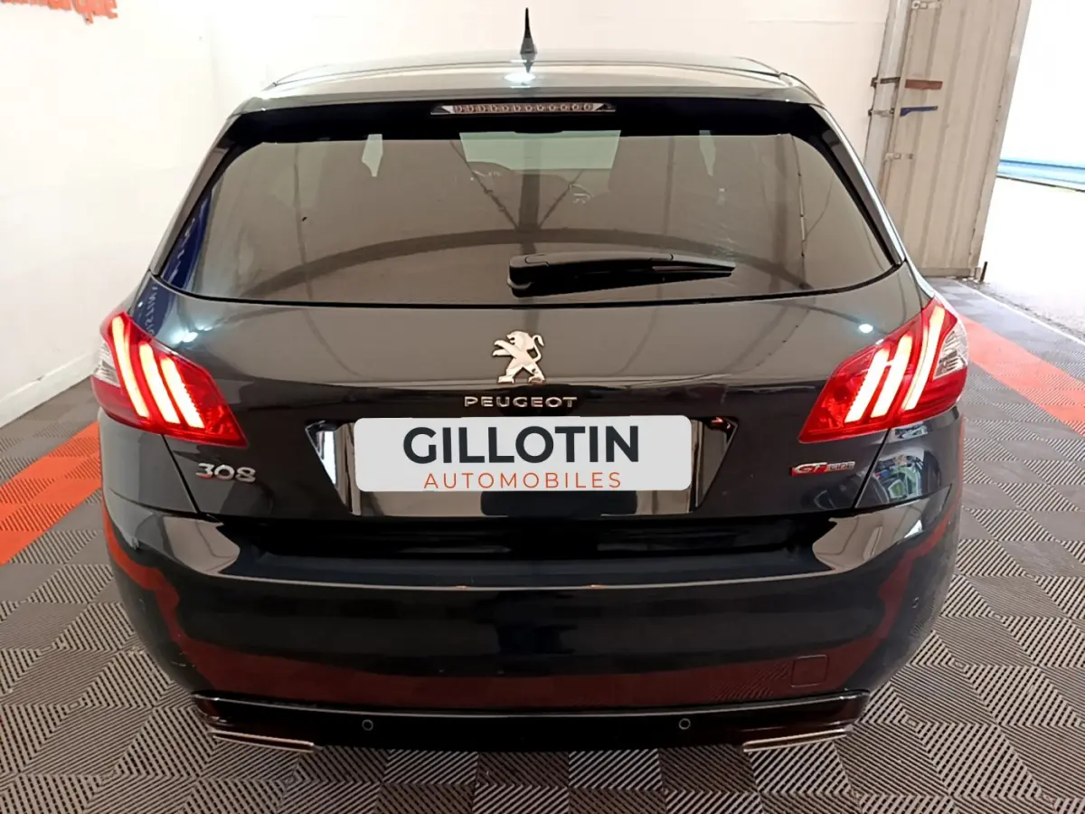 Vue arrière d'une Peugeot 308 gris foncé avec feux allumés et logo GT Line visible sur un sol à damier.