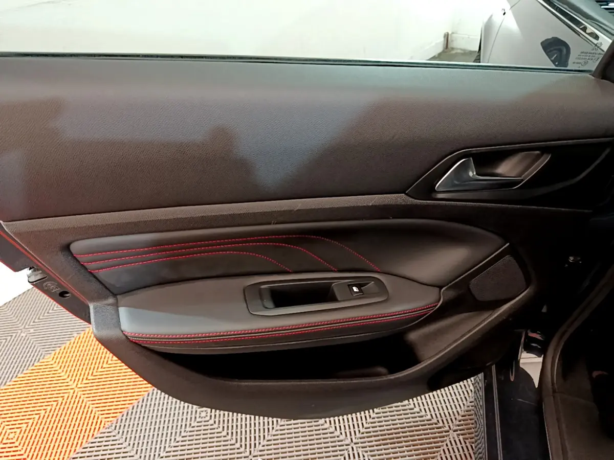 Vue rapprochée de la porte intérieure côté gauche d'une Peugeot 308 GT Line avec surpiqûres rouges et poignée noire.