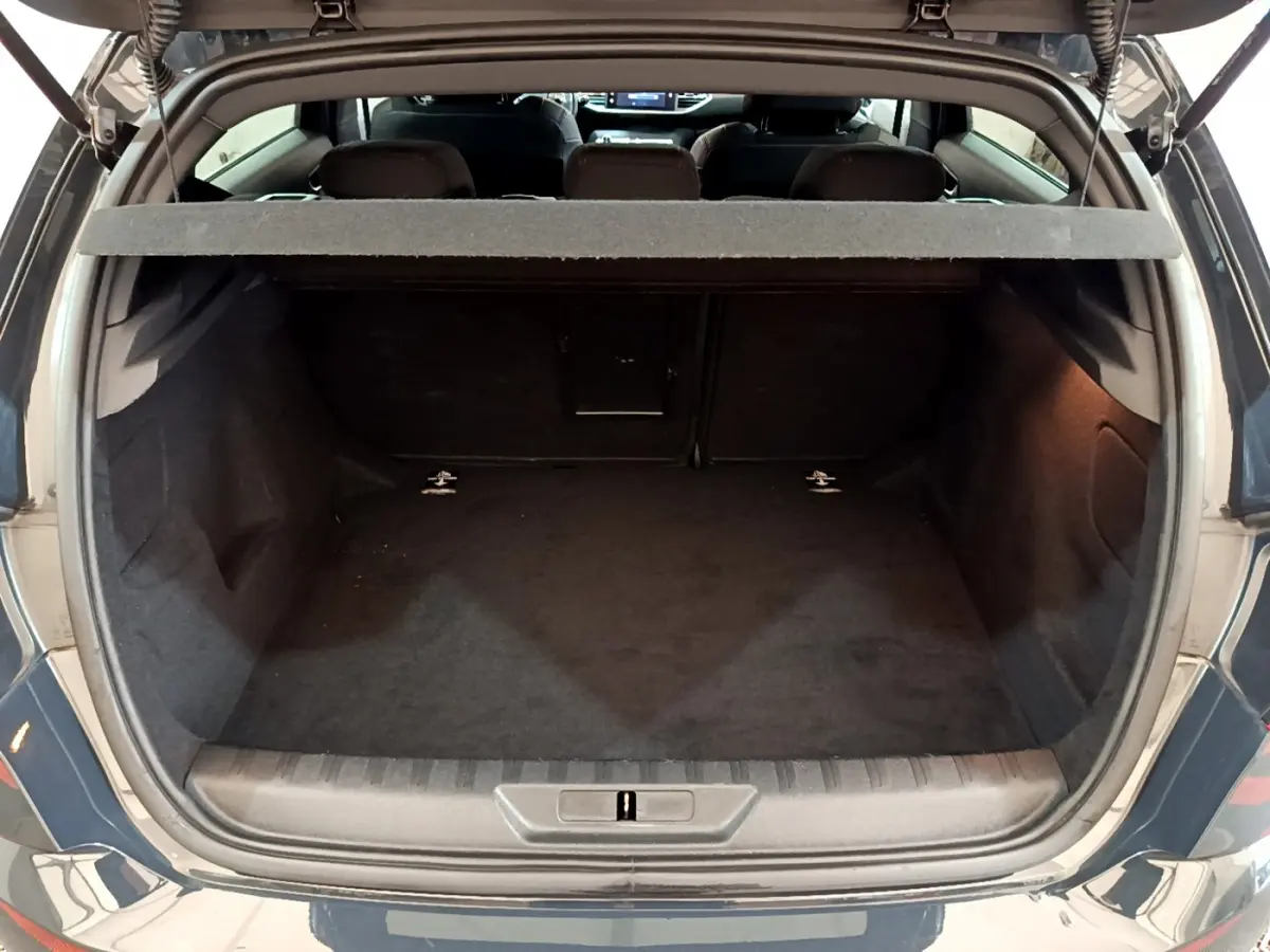Coffre ouvert vu de l'arrière d'une Peugeot 308 gris foncé, montrant la banquette arrière et la trappe à ski.